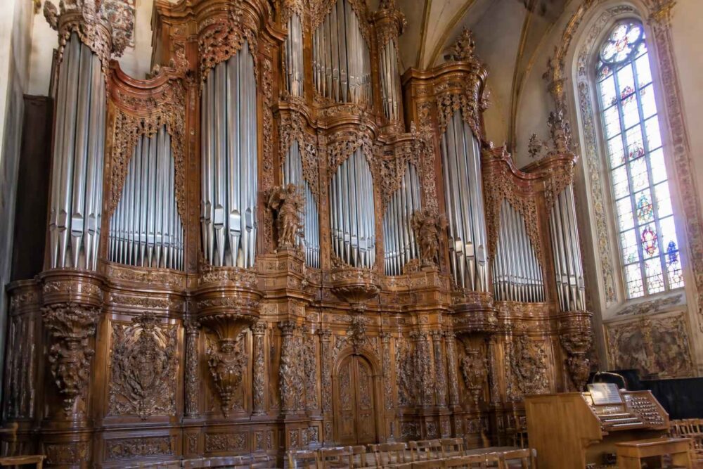 Bogato rzeźbiona barokowa empora organowa Monumentalne piszczałki organowe w dekorowanej drewnem barokowej części kościoła obok wysokiego witraża