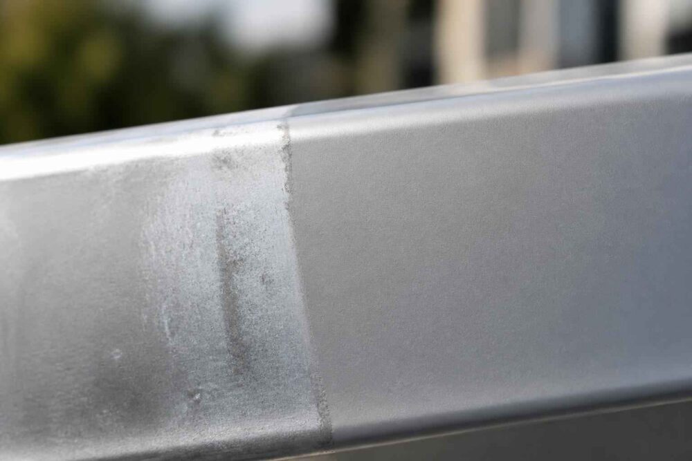 Zbliżenie na zmatowiały i zabrudzony fragment metalowej balustrady przed budynkiem